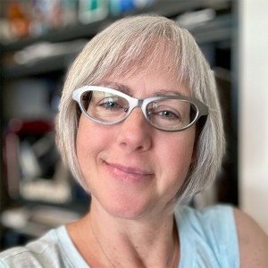 A woman with silver framed glasses and silver hair, smiling. Her name is Leesa JoAnn Iverson
